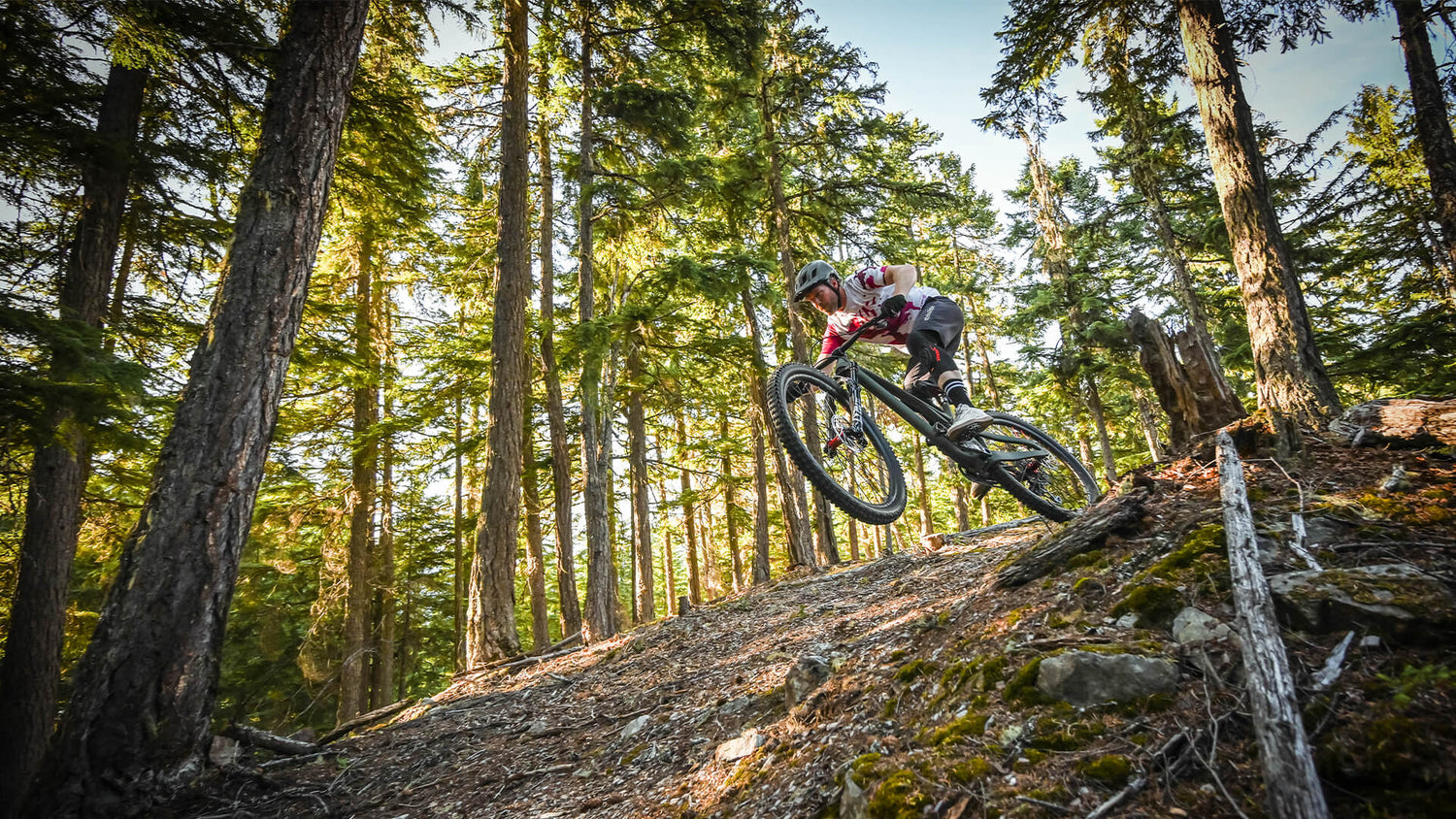 Mountain bike rider going down a trail, passing trees wearing our Flowline gear